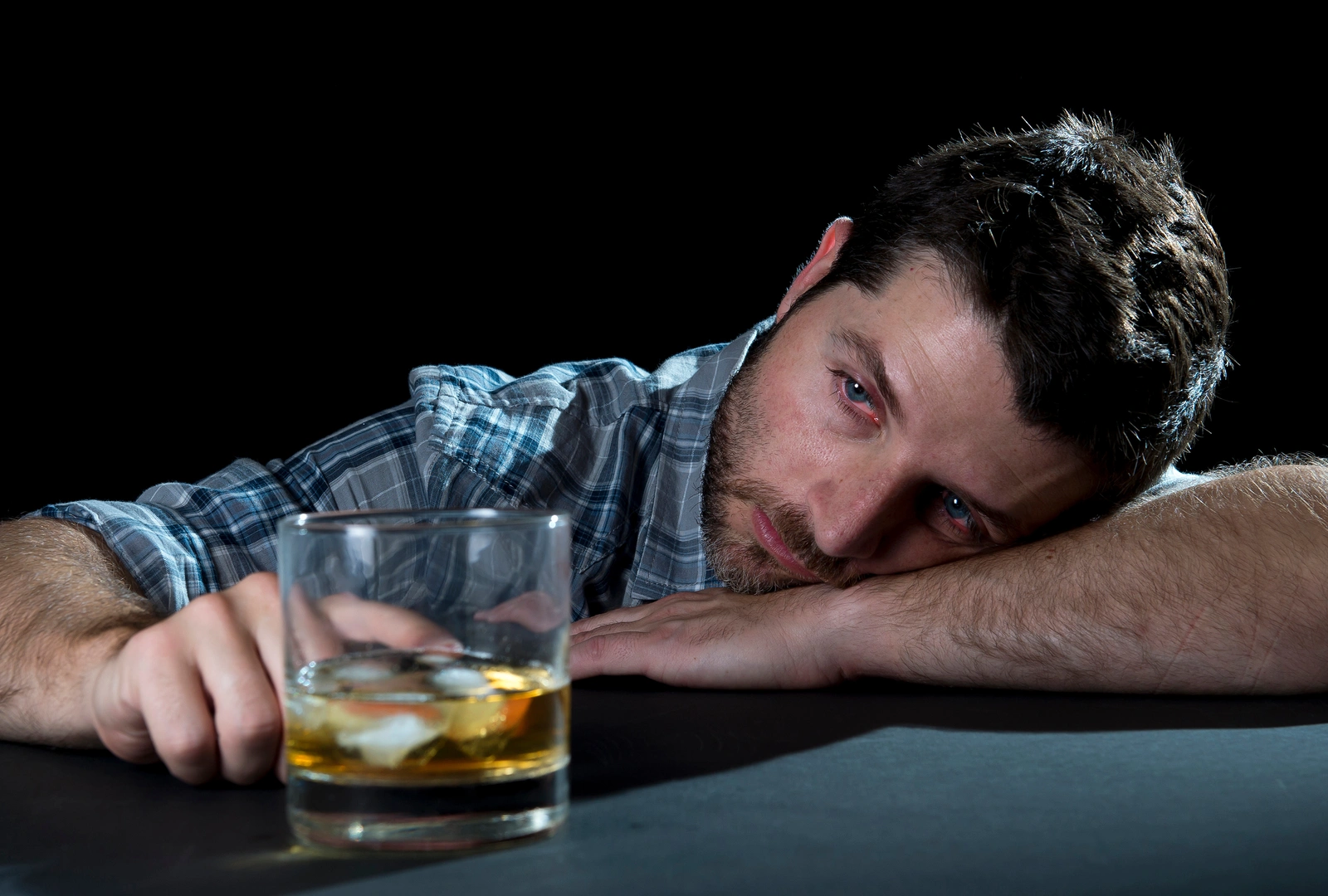 a man laying his head on a bar top looking sick and staring at his alcoholic beverage